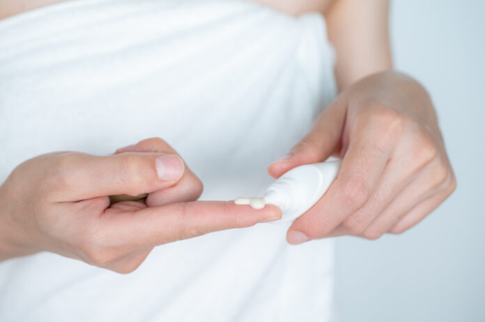 Cropped shot view of woman squeezing out cream from cosmetic tube.